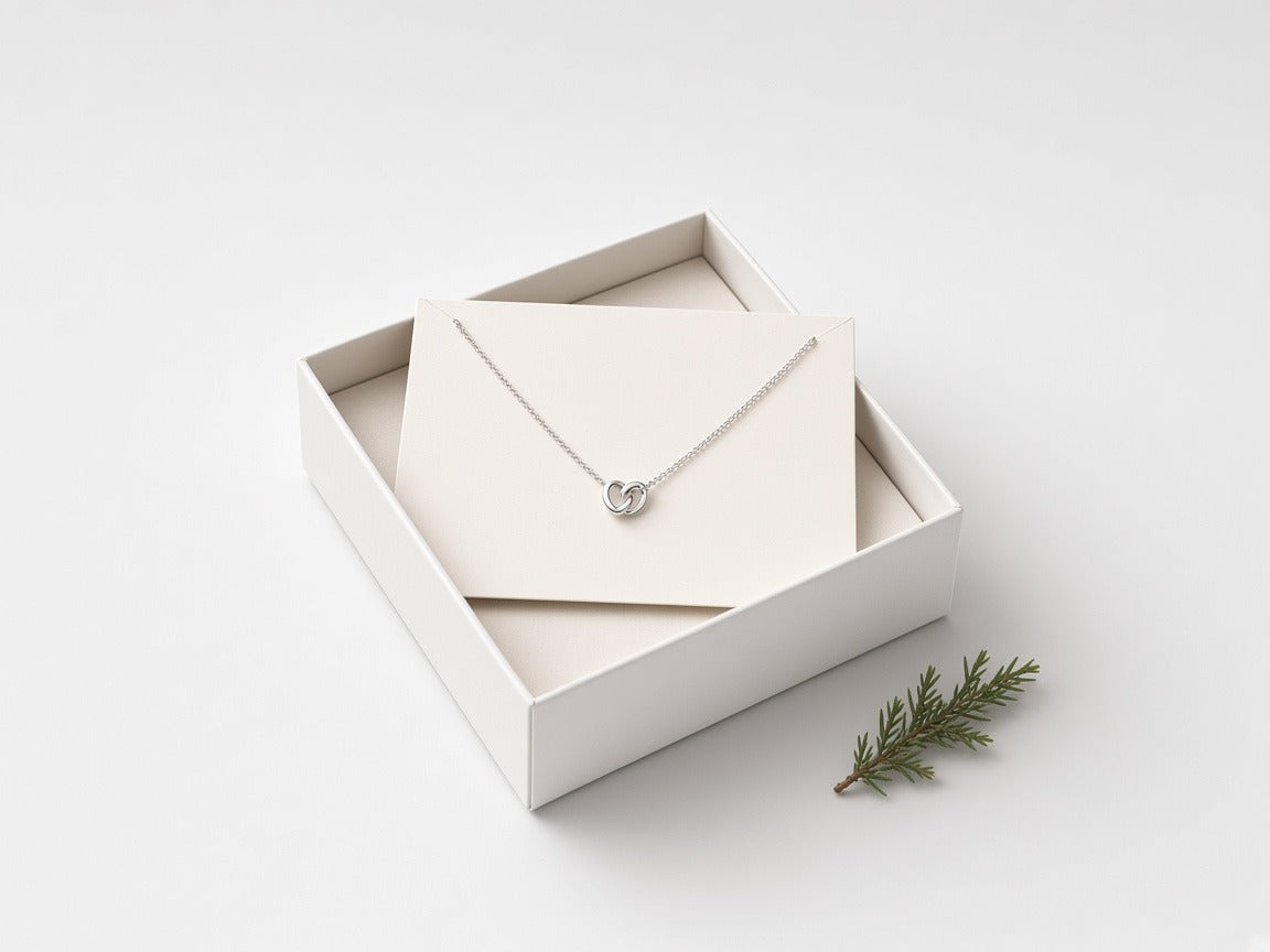 Silver heart necklace on a message card in a white gift box with a sprig of evergreen